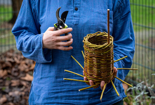 Craftswoman making woven bird house, weaving wicker basket from willow branches