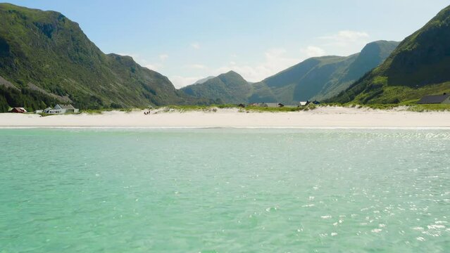 Cinematic aerial establishing shot, low drone flight pull in over turquoise crystal clear water towards a white beach shore line mountain background Summer vacation Refviksanden Norwegian Coast M&aring;l&oslash;y 