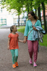 Mother and daughter hand in hand, having a conversation on a tranquil park path.
