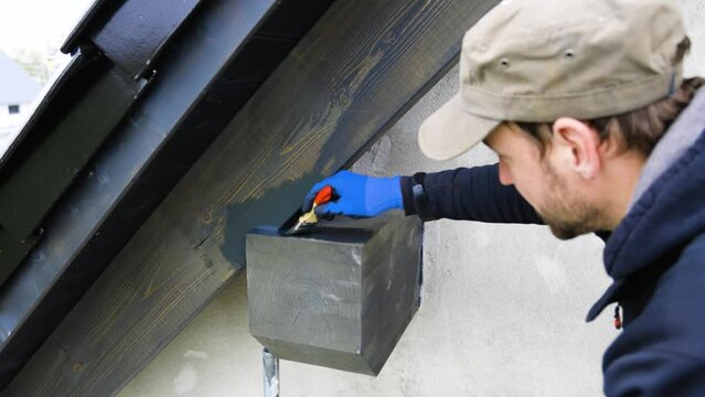Man Using a Brush to Apply Protective Coating to a Roof Beam of a House