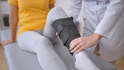 An orthopedist fits a leg brace on a patient, aiding rehabilitation after a sprain injury - obrazy, fototapety, plakaty