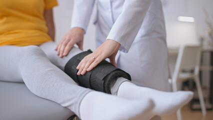 A female doctor examines the leg of a patient in a medical brace, facilitating injury healing
