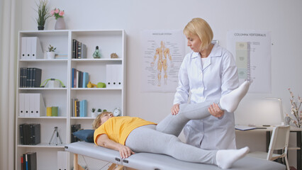 A woman orthopedist examines a patient's joints and leg muscles in a clinic, providing healthcare...