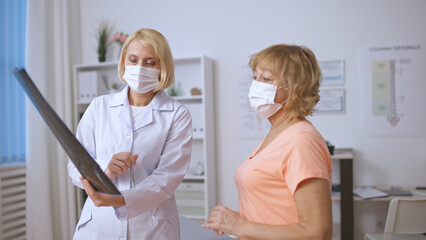 Fototapeta premium A doctor and patient discuss an X-ray image while wearing protective face masks in a clinic
