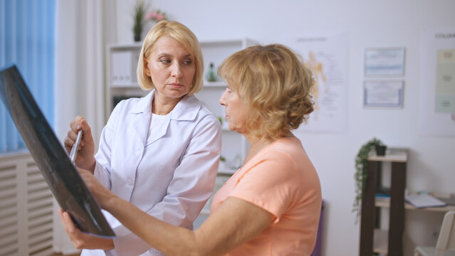 A female patient, upset about her slow recovery, asks an orthopedist about her prognosis while looking at an X-ray scan