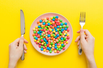the girl holds cutlery in her hands and eats sweets in a plate. Health and obesity concept, top view on colored background - obrazy, fototapety, plakaty