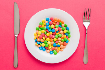 cutlery on table and sweet plate of candy. Health and obesity concept, top view on colored...
