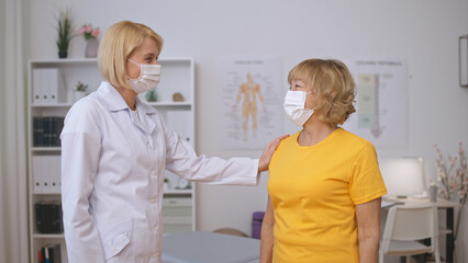 Fototapeta premium A doctor supports and congratulates a mature female patient in a face mask on her recovery