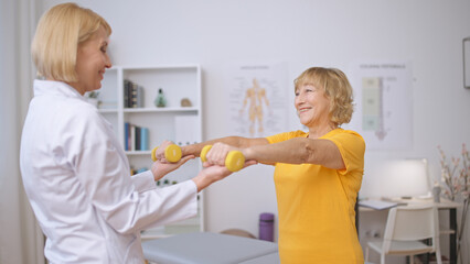 An excited patient and doctor exercise with dumbbells together at a rehabilitation clinic