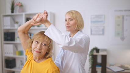 Obraz premium A masseur assists a senior lady with muscle stretching, providing treatment at a rehabilitation center
