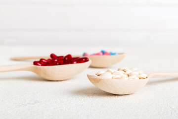 Vitamin capsules in a spoon on a colored background. Pills served as a healthy meal. Red soft gel vitamin supplement capsules on spoon