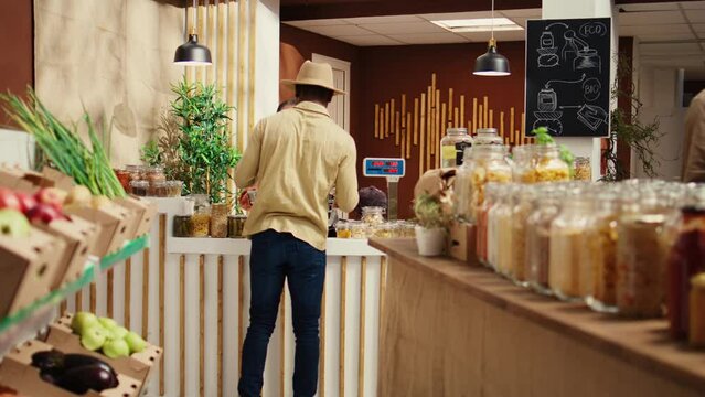 Woman scanning organic goods for client at checkout counter, selling locally grown pesticides free produce and pantry supplies. African american worker helping buyer to weight merchandise. Camera B.