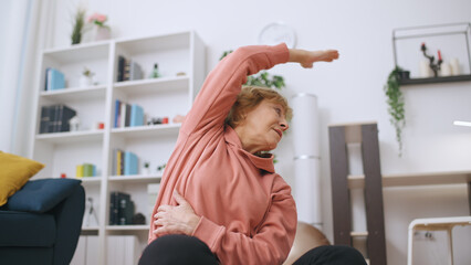A fit senior woman performs stretching exercises in front of her laptop during an online training...