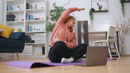 A happy, active senior female enjoys fitness training online, exercising at home
