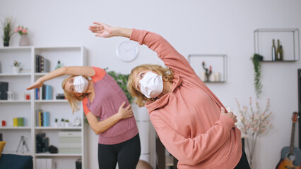 Senior and young women in medical masks exercise at home, adapting sports to the pandemic