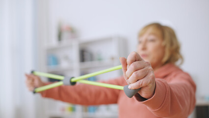 A senior woman exercises with a stretching band, committed to an active lifestyle and fitness at...