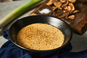 Traditional Transcarpathian Yushka with Porcini Mushrooms, Heartily Served in a Cast Iron Bowl on a Textured Blue Napkin, Accompanied by Dried Porcini and Fresh Leek on a Wooden Board