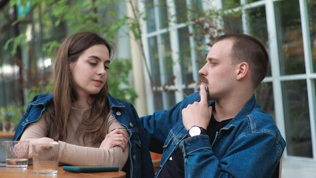 A young couple. Denim clothes. On a date in a vintage restaurant, outside. They are talking.