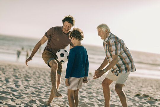 Three generations of men playing soccer on the beach