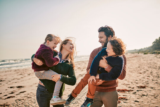 Family enjoying time together on the beach with parents carrying children