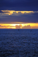 The waters of open sea are dark blue and the sky is golden, after sunset.