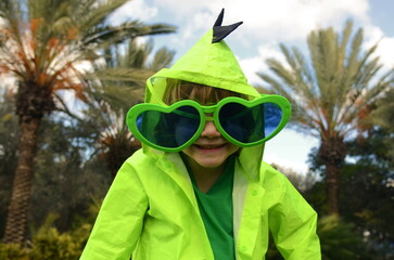 A child in a dinosaur raincoat, wearing funny heart-shaped glasses. Concept: good weather, summer...