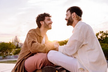 Laughing young male couple talking while sitting against blurred background