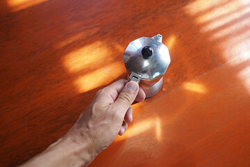 Male hand takes moka pot coffee maker on red table at sunny morning.