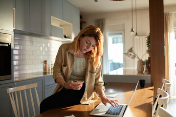 Concerned woman reviewing documents while working from her home kitchen