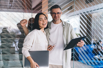 Half length portrait of Asian female and Caucasian male colleagues with modern technologies smiling...