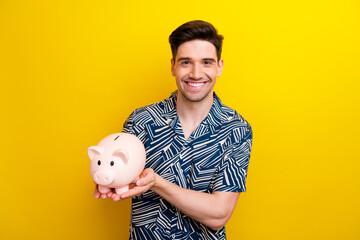 Photo of cheerful satisfied person beaming smile arms hold money pig piggy isolated on yellow color...