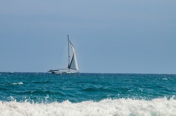 Naklejka premium Velero navegando en el horizonte en cabo de Gata, España. Yate a toda vela navegando en las aguas turquesas del Mar Mediterráneo.