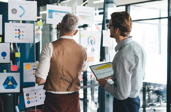 Male employees working on project attaching charts to glass wall - Powered by Adobe