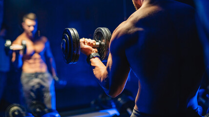 Muscular man doing exercises with dumbbells in the gym - obrazy, fototapety, plakaty