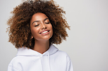 Beauty portrait of african american woman with clear healthy skin wearing white pullover hoodie .Smiling dreamy beautiful black woman. Curly hair in afro style.