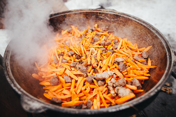 Outdoor Traditional Cooking Meat and Carrots Fried in Cauldron Over Open Fire