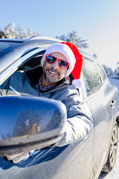 Portrait of cheerful driver with santa claus hat and sunglasses on winter day.
