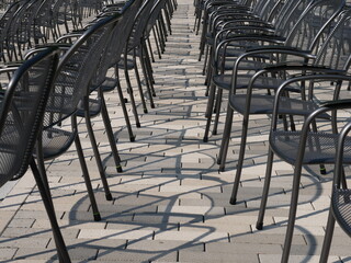 Metal stacking chairs in rows on paving stones cast interesting shadows on the ground, waiting for a large crowd of people