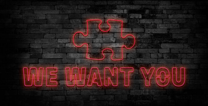 We want you neon sign in the speech bubble with a puzzle piece on brick wall background.