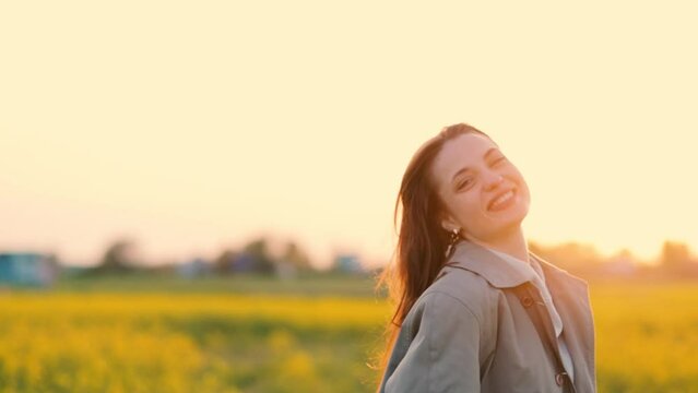 young woman smiles joyfully in the summer in a field at sunset in a jacket. A beautiful woman model enjoys life.