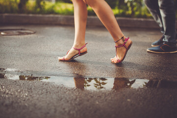 Couple walking on wet pavement, feet in sandals, flip-flops, and shoes.