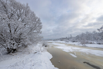 A river covered with ice and snow with thawed patches in the foreground, a winter landscape and a...