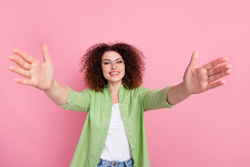 Portrait of pleasant girl with wavy hairdo wear green shirt in eyewear stretching arms to hug you isolated on pink color background