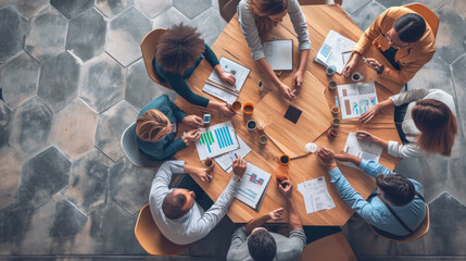 top-down view of a diverse group of professionals engaged in a meeting around a hexagonal wooden table with documents and a central potted plant