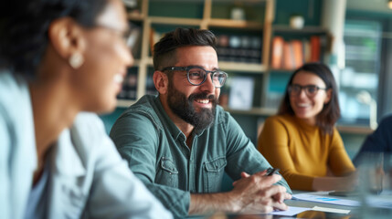 A bearded man in glasses enthusiastically discusses with colleagues during a team meeting at a vibrant office environment.