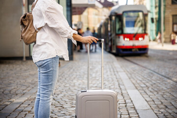 Travel by public transportation in city. Woman tourist with suitcase and backpack waiting for tram on street