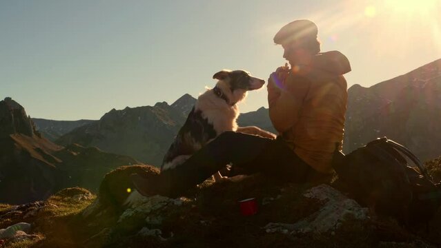 Male hiker sitting during a snack break sharing his food with his border collie dog. Sports and outdoor activity