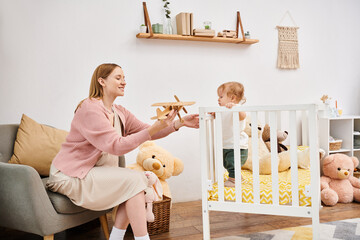 cheerful pregnant woman holding toy plane near cute toddler son in nursery room at home, motherhood