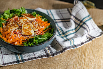 green salad with greek pan fried cheese served on wooden background with kitchen cloth textile napkin
