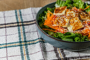green salad with greek pan fried cheese served on wooden background with kitchen cloth textile...